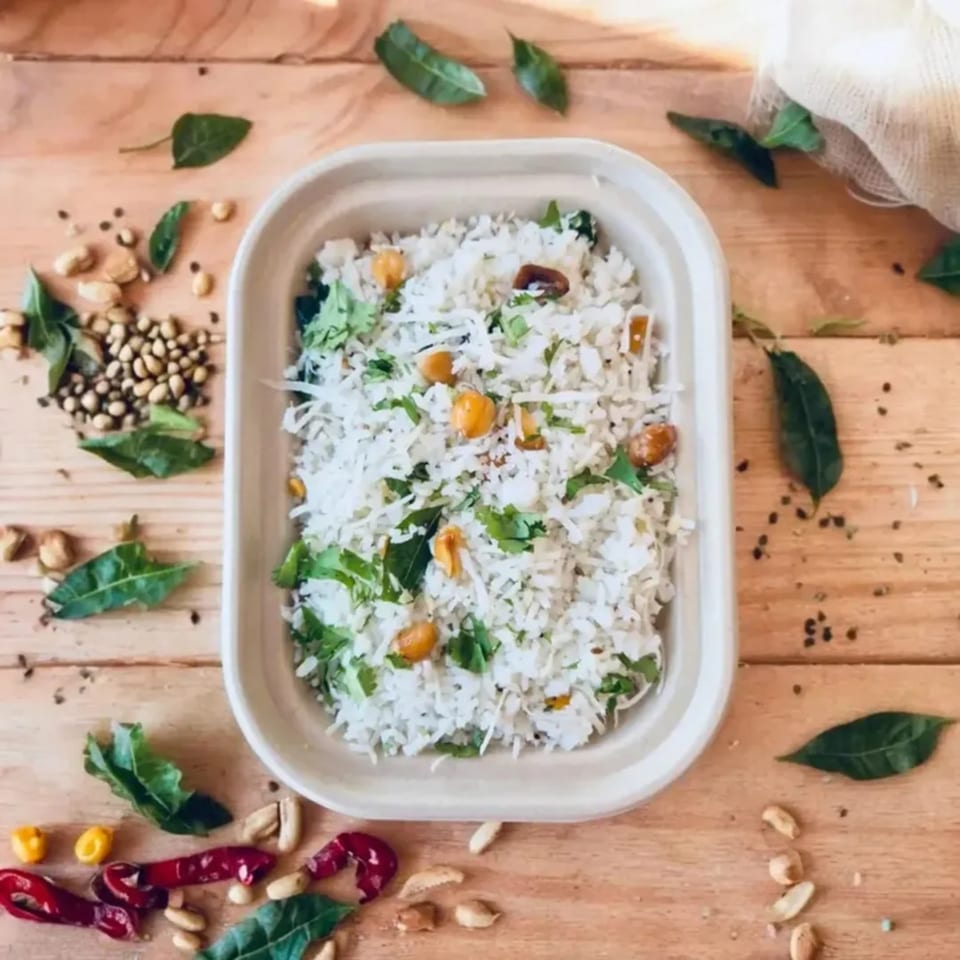 Indian coconut rice with peanuts and herbs in a white container on a wooden table.