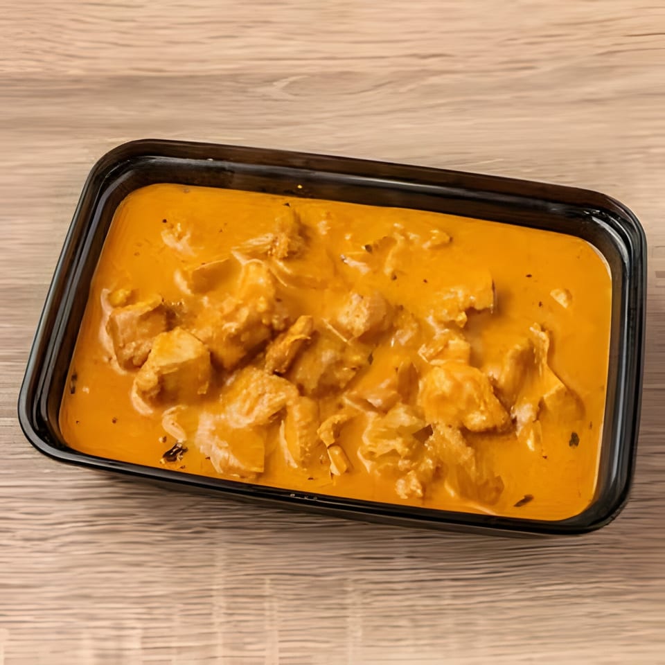 Indian chicken curry in a black rectangular takeout container on a wooden table.