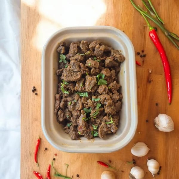 Kolapasi Indian Canteen's Indian beef fry, garnished with cilantro, on a wooden board with chilies and garlic.