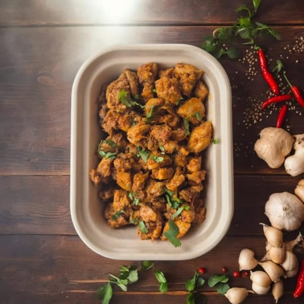 Indian chicken curry in a white container, garnished with cilantro, surrounded by spices.