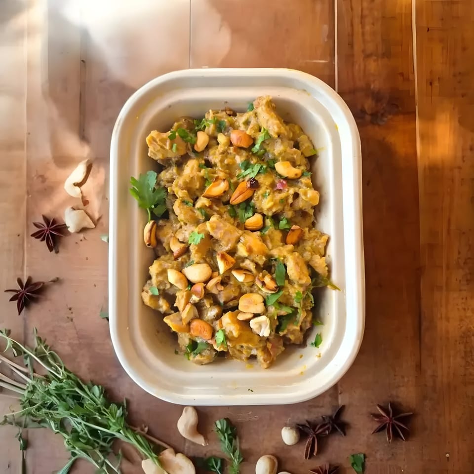 Kolapasi Indian Canteen's creamy chicken curry with cashews and cilantro, surrounded by spices.