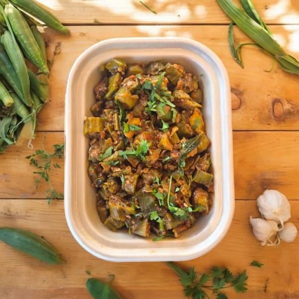 Kolapasi Indian Canteen's spicy okra curry in a white container, garnished with fresh cilantro.