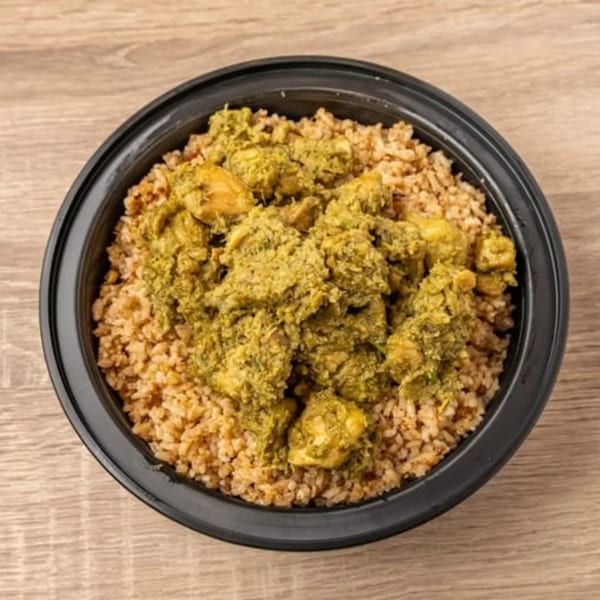 Indian green chicken curry with rice in a black bowl on a wooden table.