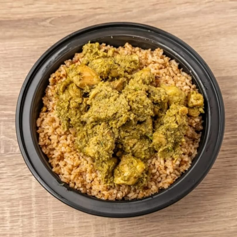 Indian green chicken curry with rice in a black bowl on a wooden table.