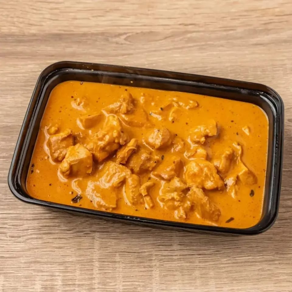 Indian chicken curry in a black rectangular container on a wooden table.