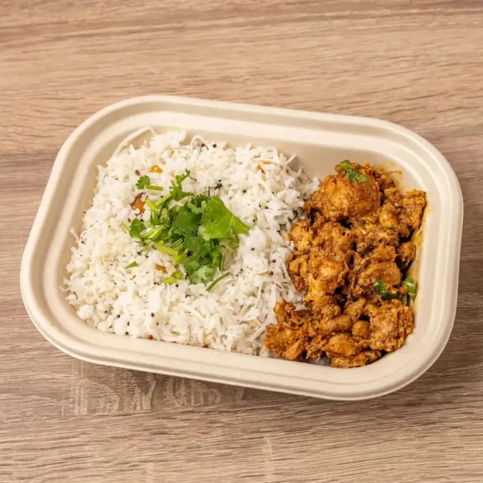 Indian chicken curry with white rice and cilantro in a takeout container on a wooden table.